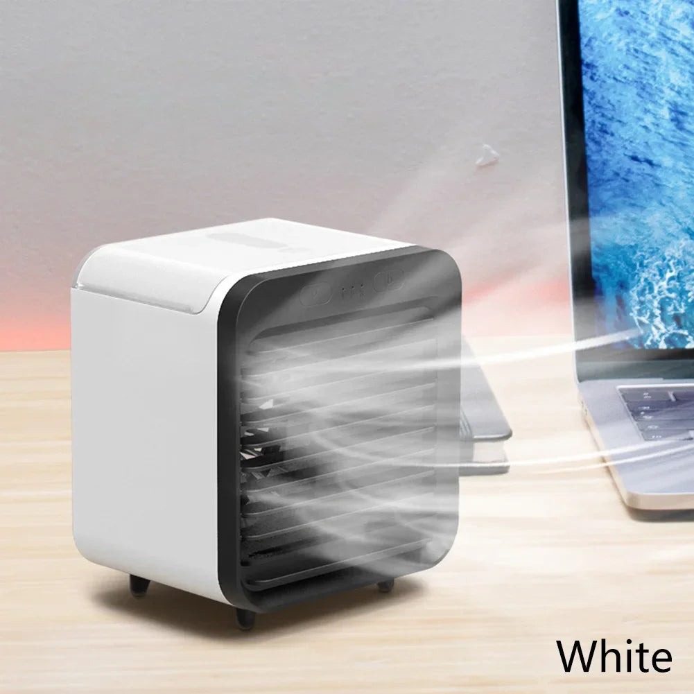 White compact rechargeable mini air cooler and humidifier blowing mist, next to a laptop.